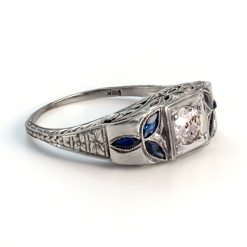 Angled interior view of an 18k white gold Art Deco shield ring showing the gold hallmark and intricate foliate sapphire shoulders.