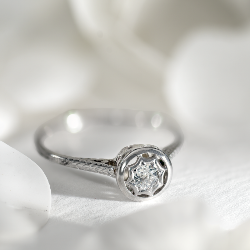 Editorial shot of a 1940s 14k white gold ring with a transitional diamond in a starburst bezel and engraved shoulders.