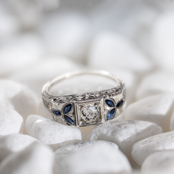 Lifestyle view of an Art Deco 18k white gold target ring featuring a 5mm central diamond and marquise sapphire accents on white stones.