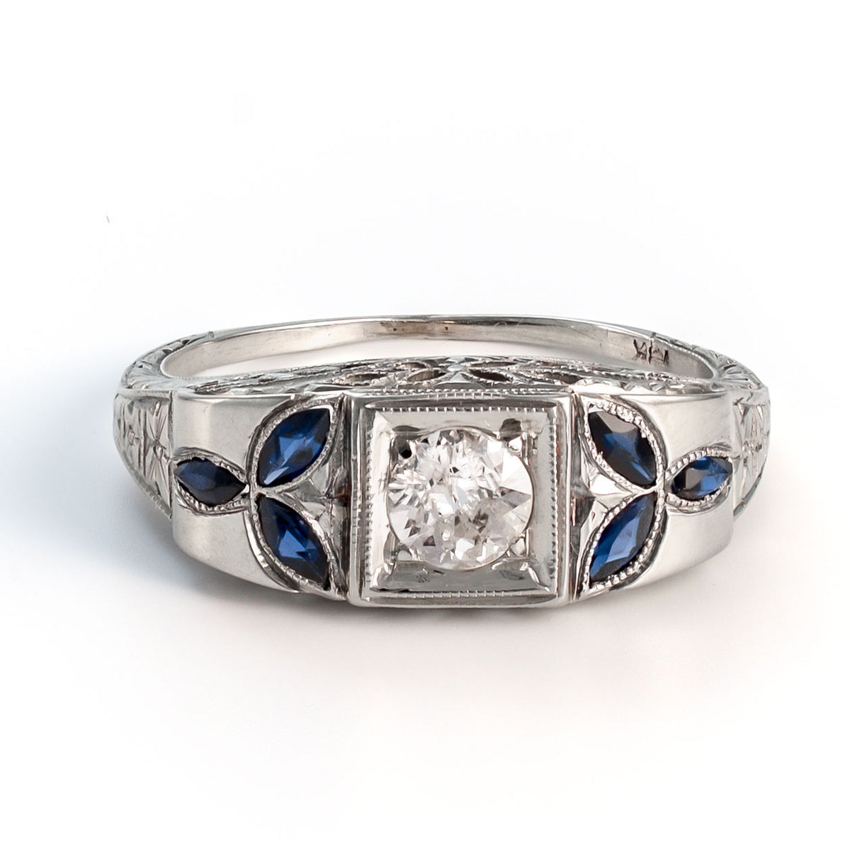 Close-up view of an 18k white gold shield ring featuring a 5mm central diamond and symmetrical marquise sapphire foliate accents.