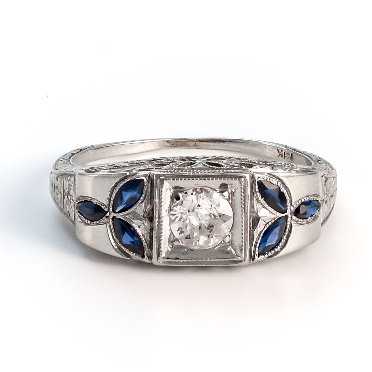 Close-up view of an 18k white gold shield ring featuring a 5mm central diamond and symmetrical marquise sapphire foliate accents.
