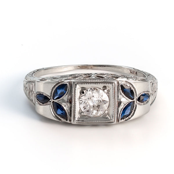 Close-up view of an 18k white gold shield ring featuring a 5mm central diamond and symmetrical marquise sapphire foliate accents.