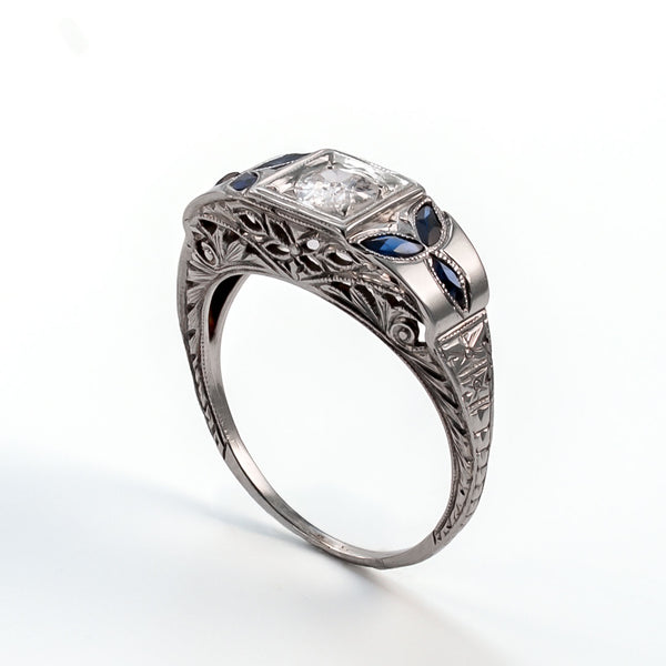 Angled profile view of an 18k white gold shield ring featuring architectural filigree, foliate sapphires, and a 5mm central diamond.