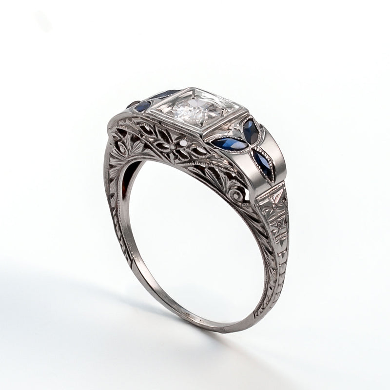 Angled profile view of an 18k white gold shield ring featuring architectural filigree, foliate sapphires, and a 5mm central diamond.