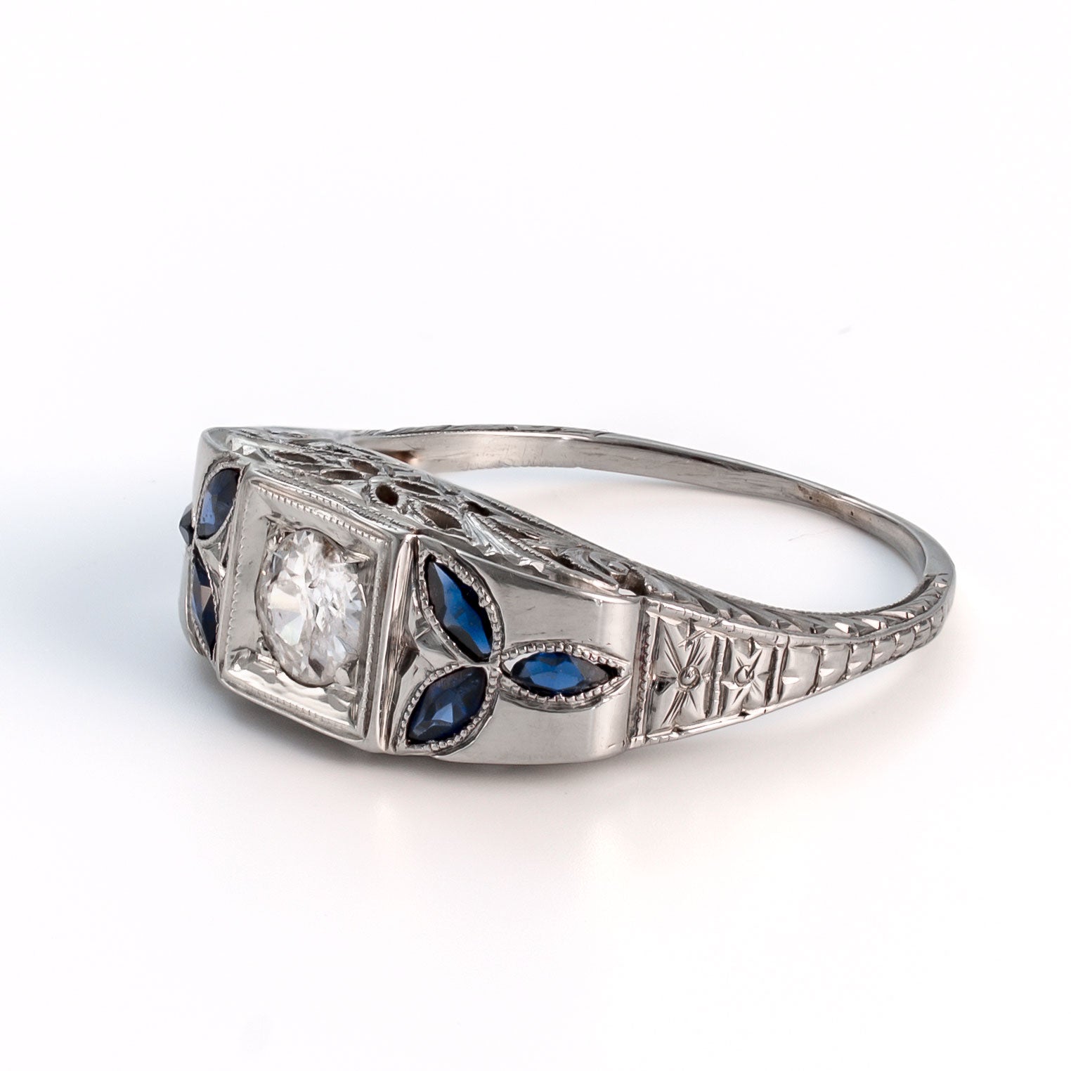 Angled profile view of an 18k white gold shield ring featuring marquise sapphire floral accents and intricate gallery filigree.