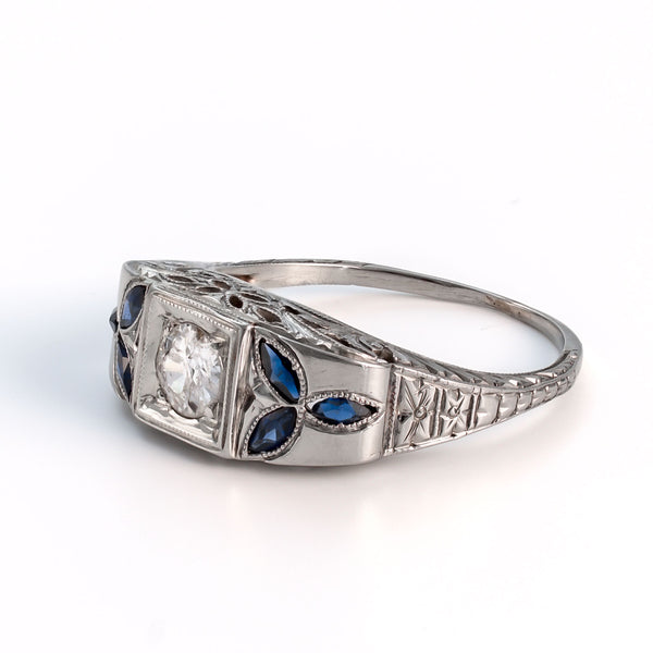 Angled profile view of an 18k white gold shield ring featuring marquise sapphire floral accents and intricate gallery filigree.