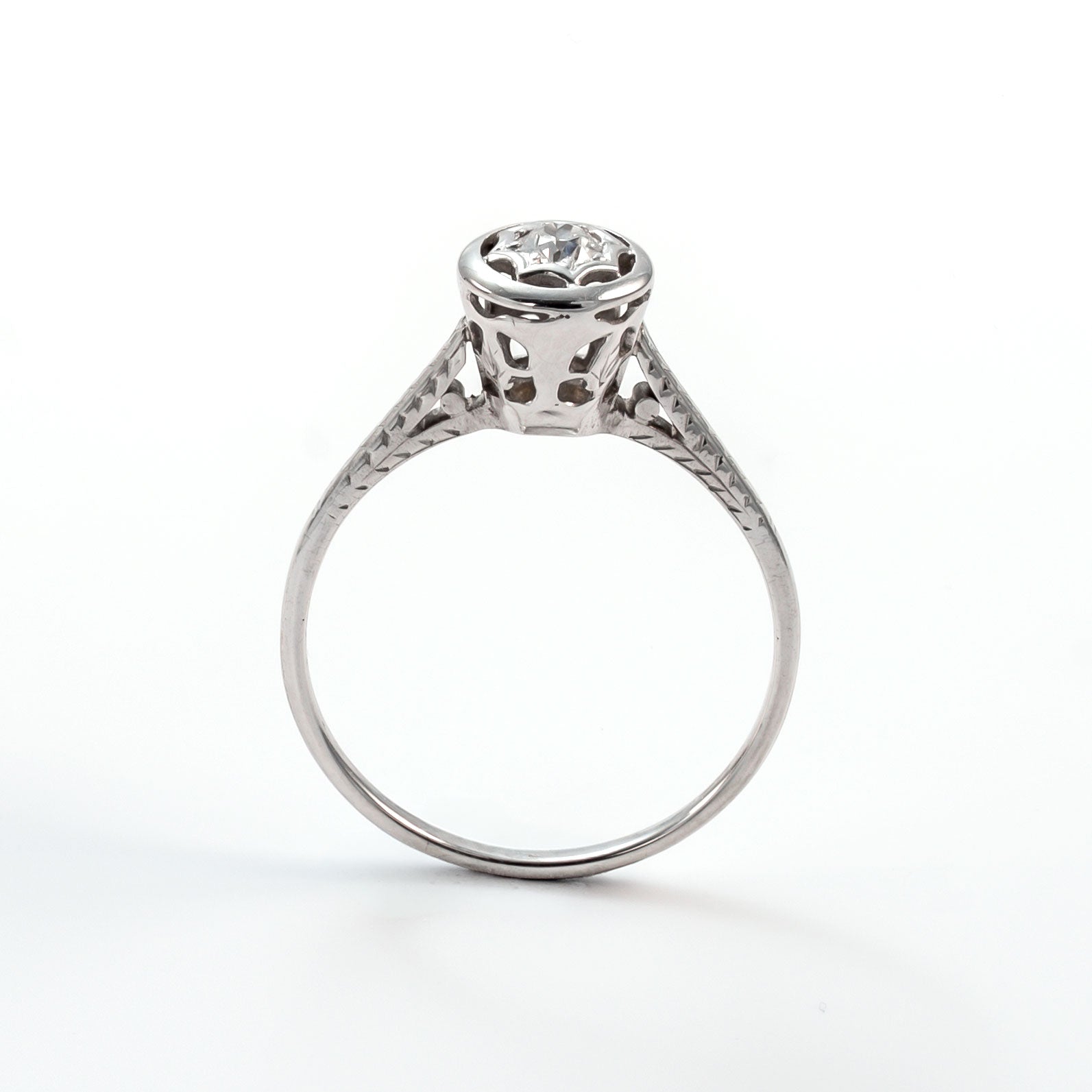 Frontal view of a 14k white gold diamond solitaire ring with an intricate star-shaped bezel and slim polished band.