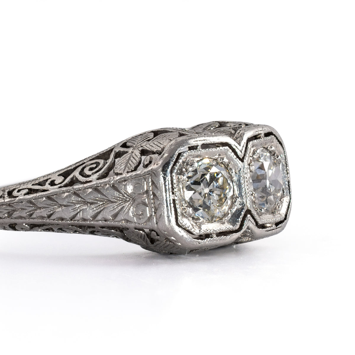 Detailed close-up of the side face of an antique two-stone platinum ring, highlighting fine bead milgrain edging and hand-chiseled leaf engravings.