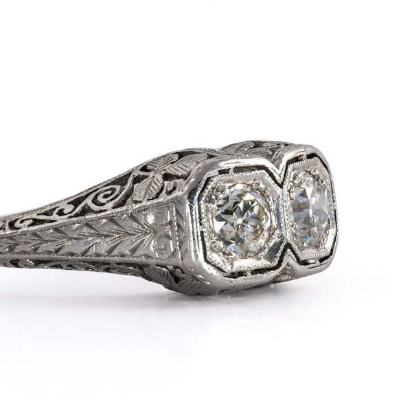 Detailed close-up of the side face of an antique two-stone platinum ring, highlighting fine bead milgrain edging and hand-chiseled leaf engravings.
