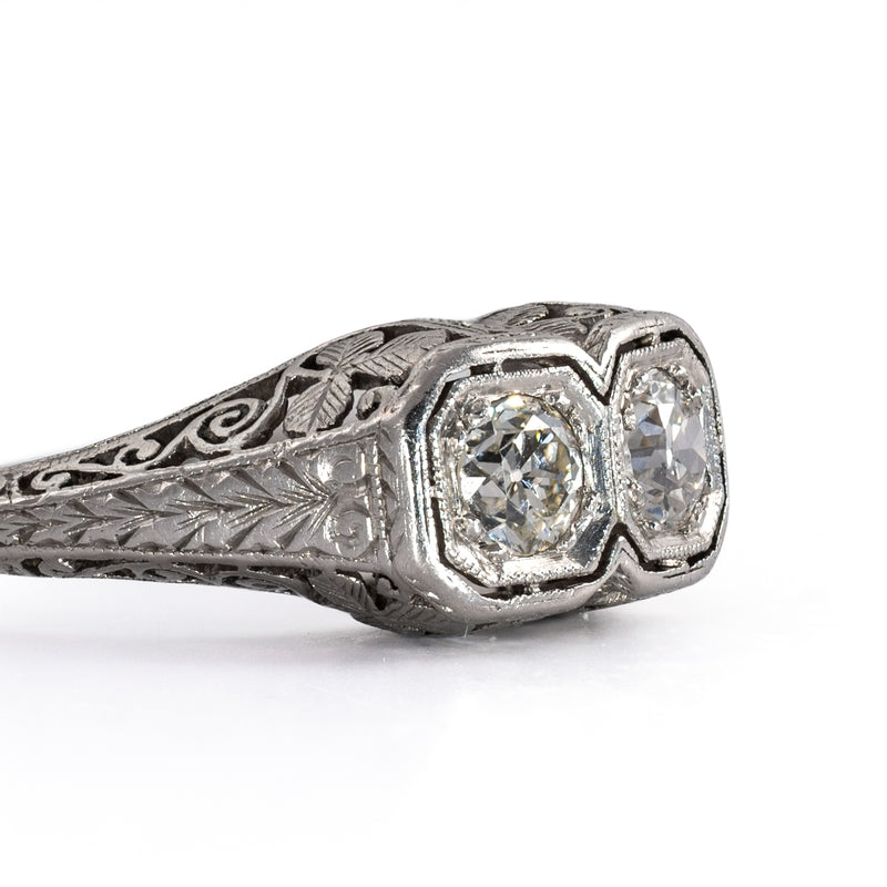 Detailed close-up of the side face of an antique two-stone platinum ring, highlighting fine bead milgrain edging and hand-chiseled leaf engravings.