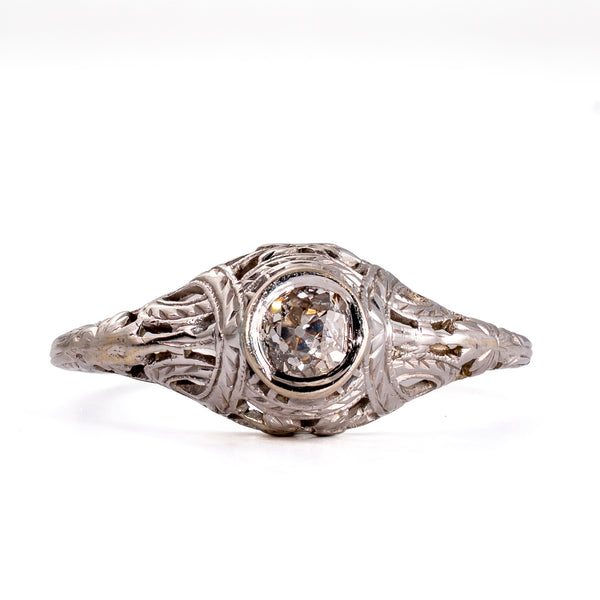 Straight-on view of an antique diamond solitaire highlighting the symmetrical bezel setting, crisp engraving, and pierced filigree.
