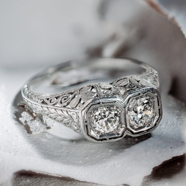 Hero perspective of an authentic 1920s Art Deco bespoke platinum Toi et Moi ring, showcasing two Old European cut diamonds in octagonal milgrain bezels resting on textured natural stone.