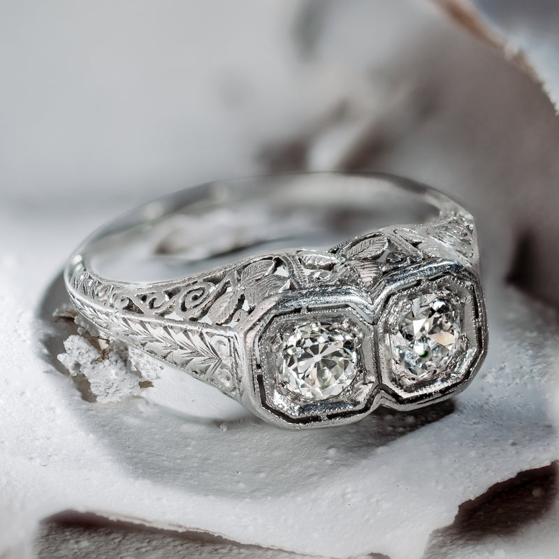 Hero perspective of an authentic 1920s Art Deco bespoke platinum Toi et Moi ring, showcasing two Old European cut diamonds in octagonal milgrain bezels resting on textured natural stone.