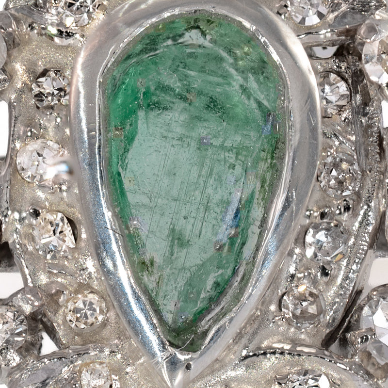Macro close-up view of natural pear-shaped emerald center stone showing jardin inclusions and bezel setting