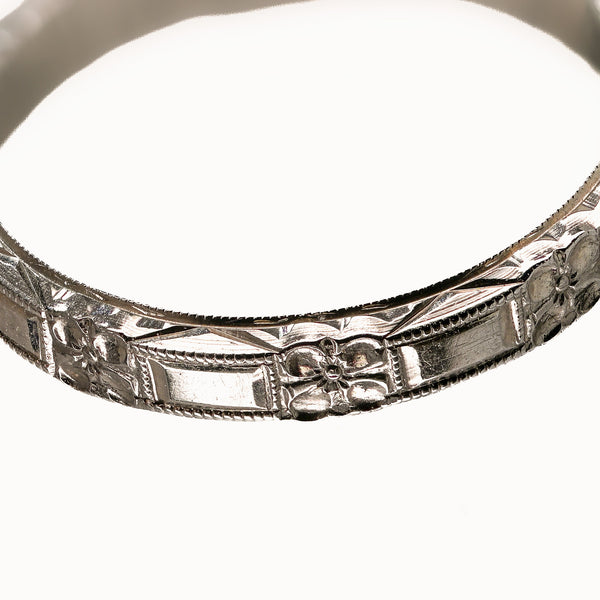 Macro detail of antique Belais 18K white gold band showing four-petal flower and beaded border engraving.