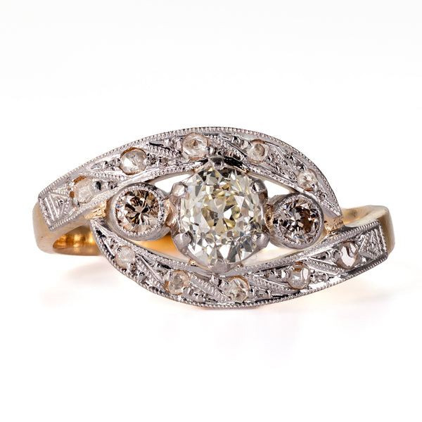 Antique Edwardian diamond bypass ring in 18k yellow gold and platinum top, featuring a central old mine-cut diamond flanked by two diamonds within flowing curves.