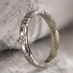 Angled profile of antique Belais 18K white gold band on stone displaying three-sided dimensional engraving.