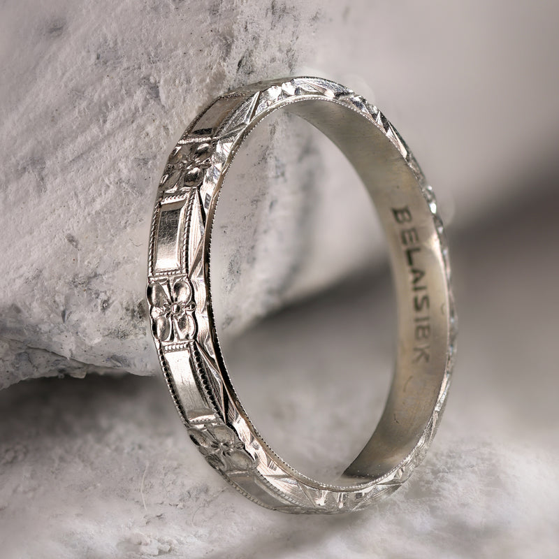 Angled profile of antique Belais 18K white gold band on stone displaying three-sided dimensional engraving.