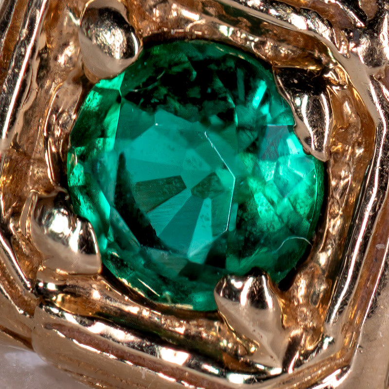 An extreme macro close-up of the round natural green emerald center stone showing faceting, internal inclusions, and gold prongs of ta vintage, Art Deco ring.