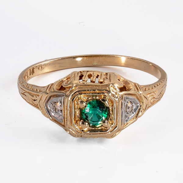 Slightly elevated front view of a vintage 1930s 14K yellow gold emerald ring showing engraved shoulders and contrasting white metal details.