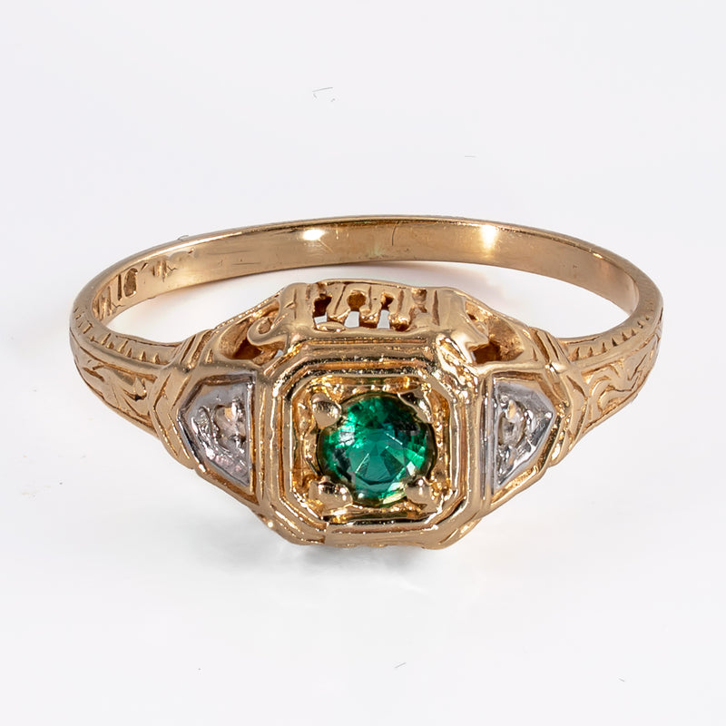 Slightly elevated front view of a vintage 1930s 14K yellow gold emerald ring showing engraved shoulders and contrasting white metal details.