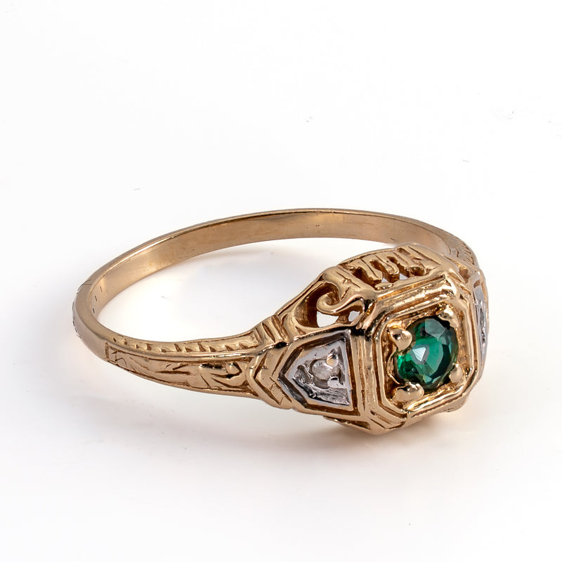 Three-quarter side perspective of an Art Deco emerald and diamond ring highlighting the openwork scrolling gallery and polished gold band.
