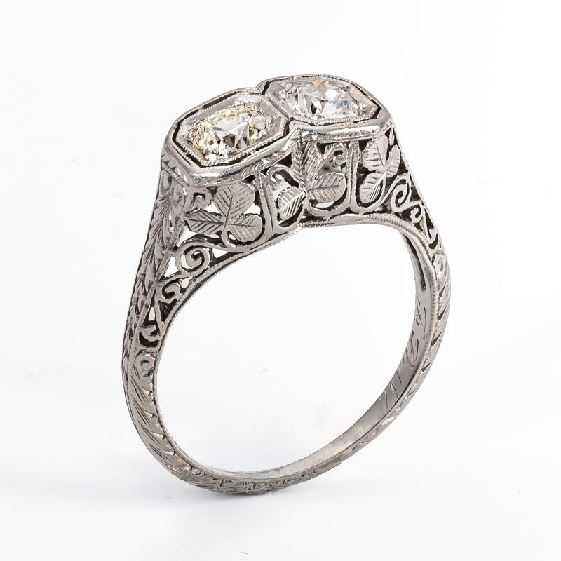 Three-quarter standing view of a 1920s Art Deco platinum Toi et Moi diamond ring showing the complete engraved shank and openwork shamrock head.