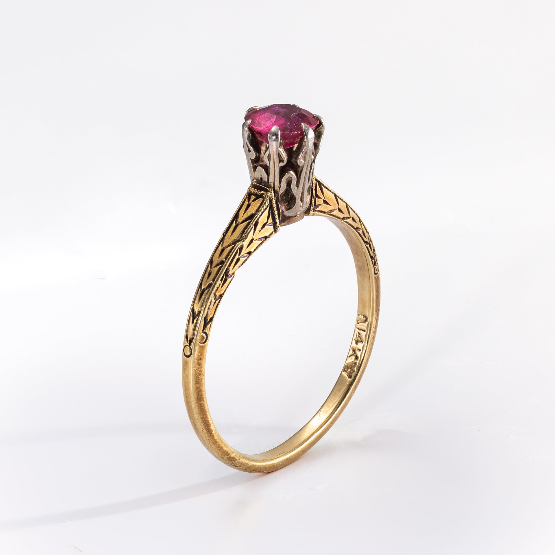 Gold ring with a central red stone on a white background